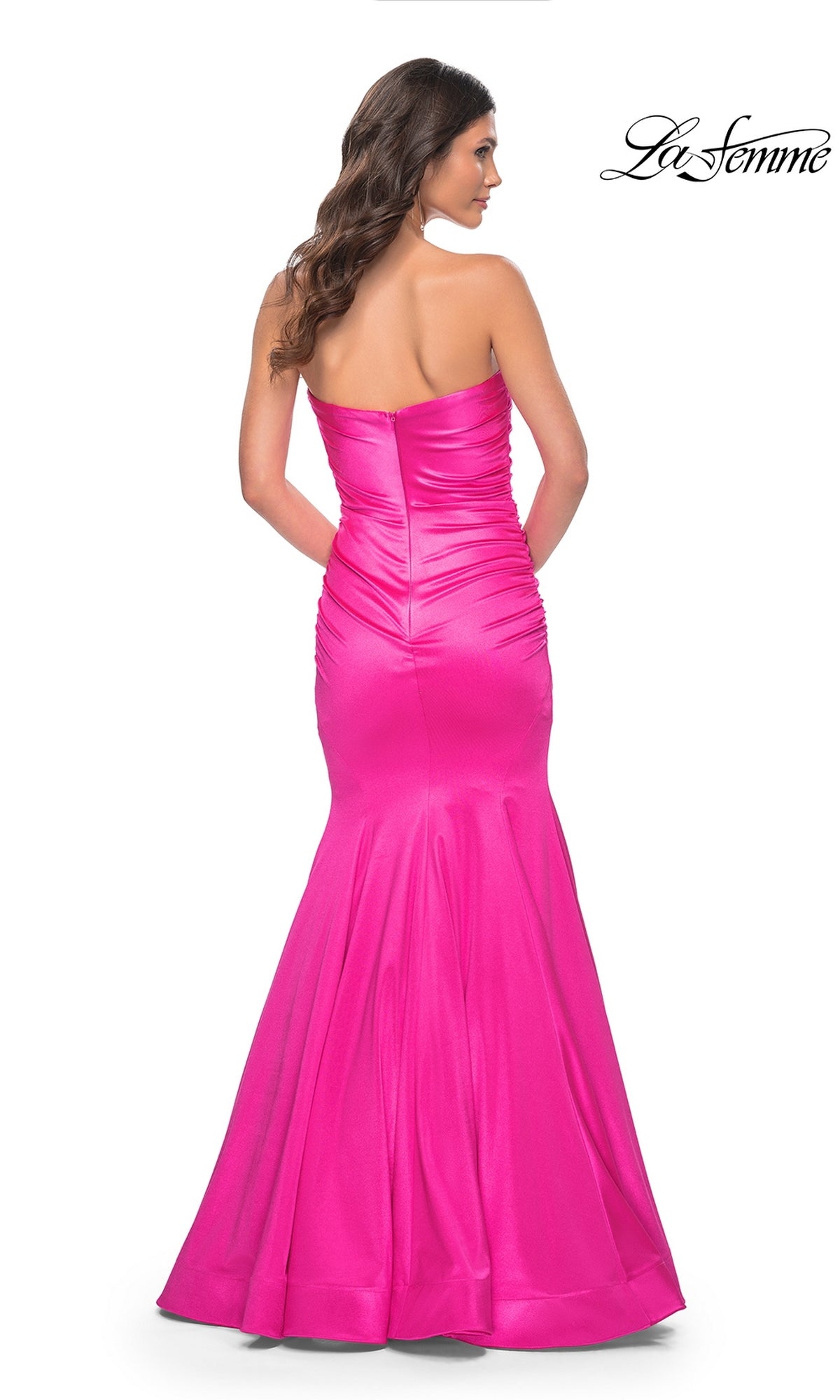 A woman models the La Femme Strapless Long Mermaid Prom Dress 31980 in hot pink, featuring a fitted, floor-length silhouette with flared hem, ruched detailing, zipper closure, and shown from the back.